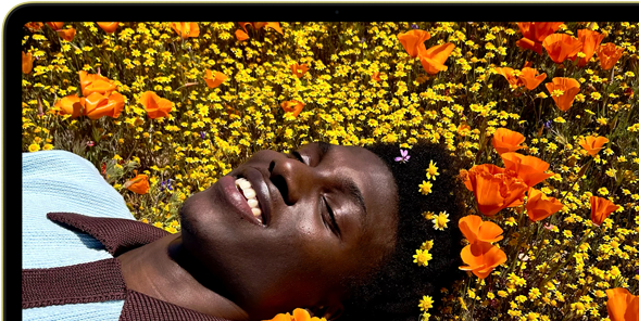 MacBook Neo, kleur Citrus, op het scherm een lachende persoon die in een zonnig bloemenveld ligt