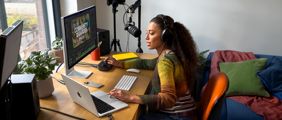 Een vrouw werkt thuis aan haar bureau met een MacBook Pro die is verbonden met twee externe displays, ze draagt oortjes en praat in een microfoon